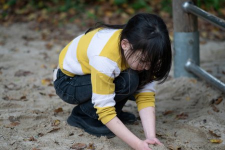 Little girl playing on the playground in the park. She is wearing a yellow jacket.