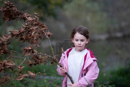 Little girl in autumn park with dry branch of tree in her hand