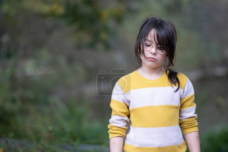 Little girl in a yellow sweater and glasses on a walk in the park