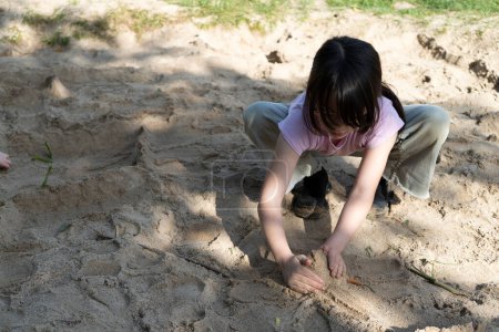 Asian girl playing in the sand at the playground in the park.