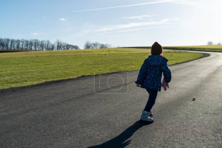 Little girl standing on the road, looking at the horizon, back view
