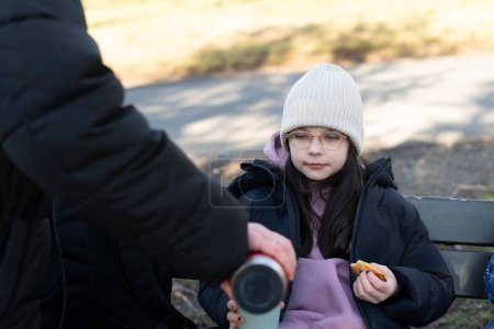 Kleines Mädchen sitzt mit ihrem Vater auf einer Parkbank und isst Kekse.