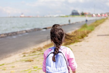 Back view of a young girl walking along the seashore.