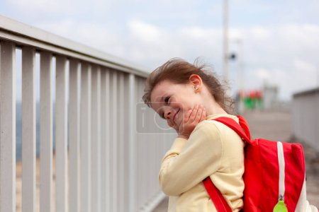A young girl with a red backpack on the street. The girl is surprised.
