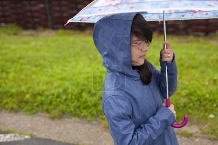 Téléchargez les photos : Asiatique petite fille en imperméable et lunettes debout avec parapluie au jour de pluie. - en image libre de droit