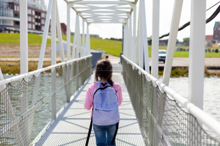 Vue arrière d'une jeune femme marchant sur un pont au-dessus d'une rivière