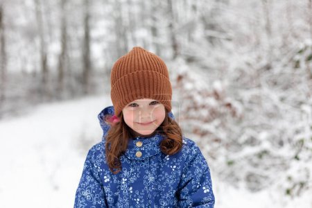 Portrait of a cute little girl in a blue jacket and hat in the winter forest
