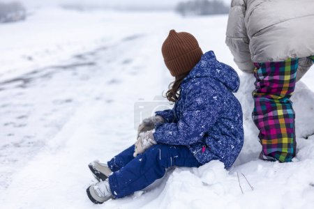 Cute little girl and her mother playing in snow on winter day