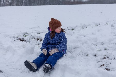 Little girl playing in the snow on a sunny winter day. She is wearing a warm hat and blue jacket.