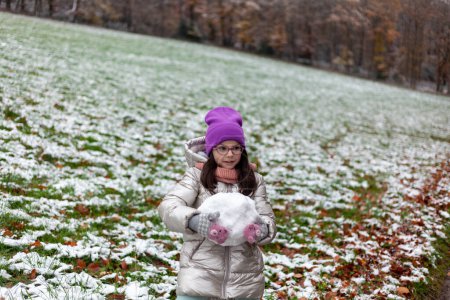 Cute little girl making snowman in the park on cold winter day