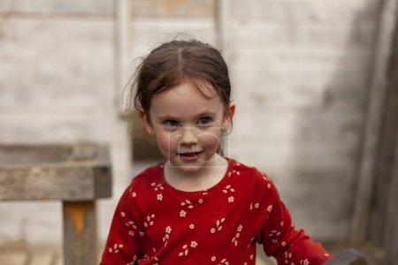 Téléchargez les photos : Petite fille surprise dans un t-shirt rouge à manches longues sur le terrain de jeu - en image libre de droit