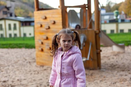 Ein kleines, warm gekleidetes Mädchen mit zwei Pferdeschwänzen spielt auf dem Spielplatz
