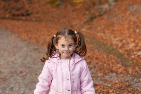 Nettes kleines Mädchen in einer Jacke mit zwei Pferdeschwänzen vor dem Hintergrund von Herbstlaub