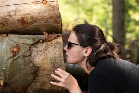 A young girl in sunglasses engaging with the natural environment by exploring the scent of freshly cut tree trunks in a forest setting