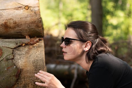 Una joven hermosa chica en gafas de sol se ve con sorpresa en los troncos de árbol recién cortados