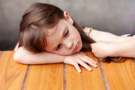 Una niña cansada yace en una mesa en un café de la calle