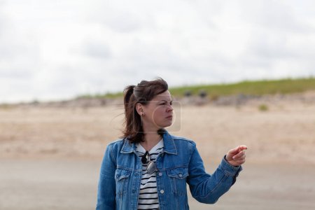 Cute girl in a denim jacket stands and looks into the distance on the beach