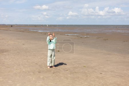 Kleines Mädchen in Kleidern fliegt einen Drachen am Strand