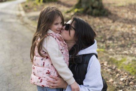 Mother kissing her daughter on the cheek in a park in springtime