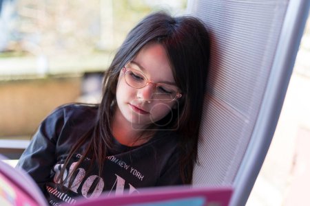 Téléchargez les photos : Jeune fille lisant un livre sur la terrasse. Concept d'éducation. - en image libre de droit