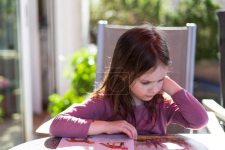 Liebenswertes kleines Mädchen liest das Buch auf dem Tisch im heimischen Garten