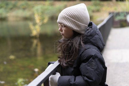 Porträt eines jungen Mädchens in Winterjacke und Hut, das ins Wasser blickt
