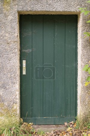 Puerta de madera verde en una pared de piedra de una antigua granja.