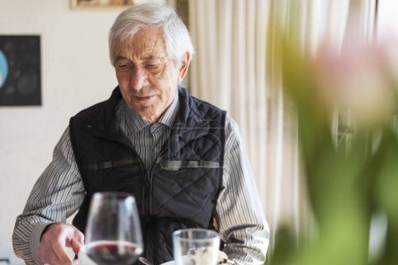 Elderly man sitting at table in restaurant and drinking red wine