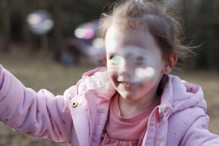 Happy little girl playing with soap bubbles in a snowless winter park