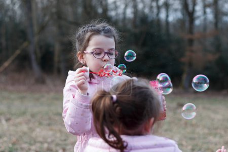 Lächelnde kleine Mädchen spielen mit Seifenblasen in einem schneelosen Winterpark
