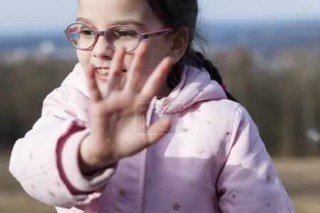 Smiling little girl in glasses playing with soap bubbles in a winter snowless park