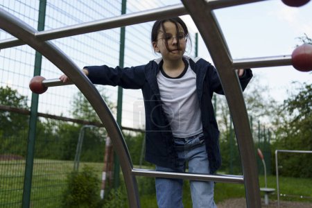 Little dark -haired cute girl climbs stairs on an open sports playground