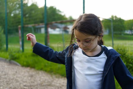 Little dark -haired cute girl walks on a rope with her hands on an open sports playground