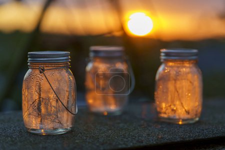 Drei solargeladene Lampen mit Girlanden drinnen in Tropfen nach dem Regen stehen auf der Terrasse in den Strahlen eines schönen Sonnenuntergangs