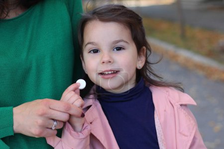 Moments d'automne : Petite fille en imperméable rose prend la médecine en plein air