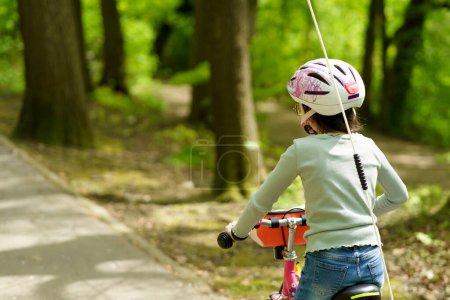 Little cute sad girl cyclist in glasses and a helmet rides through the spring park
