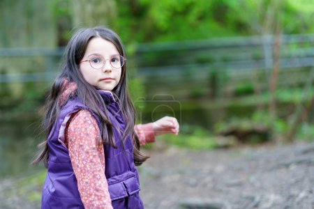 Una niña de pelo largo con gafas y un chaleco en el bosque