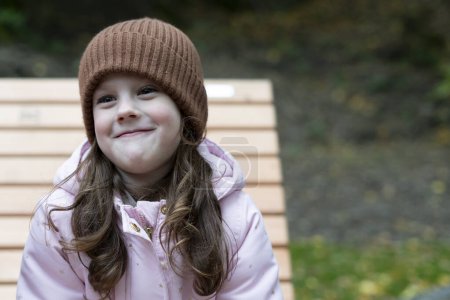 Portrait of a cute little girl on a bench in the autumn park