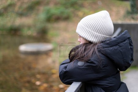 Retrato de una joven triste con chaqueta de invierno y sombrero mirando hacia otro lado en el parque de otoño
