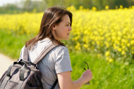 Young woman with backpack in a field of blooming rapeseed.