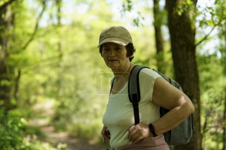 Elderly woman hiking in the forest with a backpack and hat