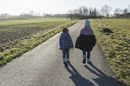 Rückansicht zweier kleiner Mädchen, die im Winter auf einer Landstraße spazieren gehen