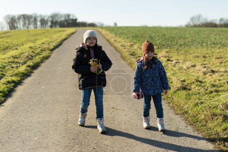 Two girls in warm clothes play on a rural road in the middle of empty snowless winter fields