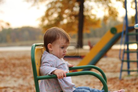 Pequeña chica hermosa paseos en un carrusel en el parque de otoño. El concepto de felicidad de los niños en la naturaleza.
