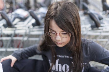 A little girl wearing glasses and a black T-shirt stands in front of supermarket carts. Customer concept