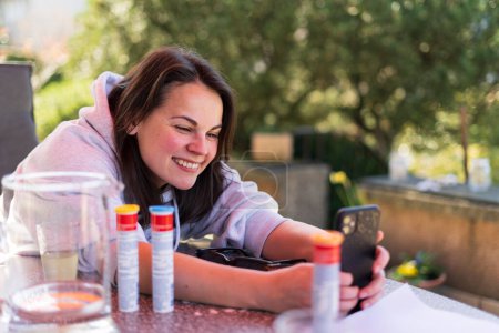 Une jolie fille souriante prend une photo sur son smartphone en lisant sur la terrasse dans l'arrière-cour de sa maison en été. Concept de bonheur familial