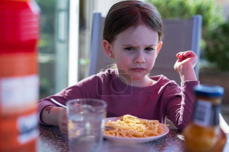 Photo for A little cute girl sits on the terrace of her house and eats pasta. Happy children's life concept - Royalty Free Image