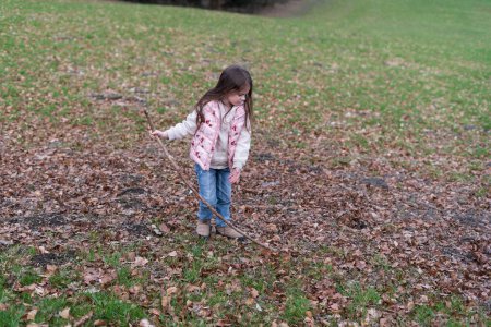 Ein kleines Mädchen rennt durch herabgefallenes Laub auf dem Rasen in einem herbstlichen Park. Glückliche Kindheit.