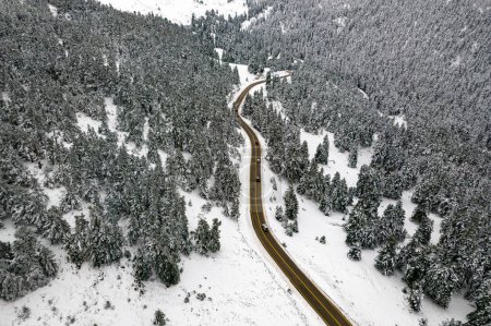 Photo for Aerial top down aerial view of a curving road crossing the slopes of Mount Parnassos with snow covering the fir trees and cars crossing the snow free road - Royalty Free Image
