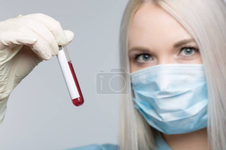 Téléchargez les photos : Jeune femme portant un masque médical et des gants médicaux manipule une sonde de sang devant un fond gris - en image libre de droit